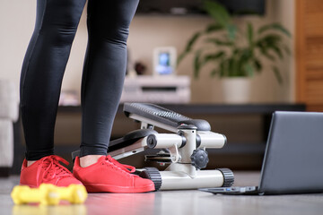 The girl turns the handle of the step simulator increases the load. Online fitness training on a step-simulator. Sports at home during the quarantine period.