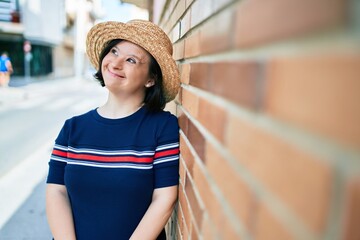 Beautiful brunette woman with down syndrome wearing a summer hat at the town on a sunny day leaning...