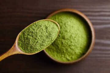 Freeze dried wheatgrass powder in spoon and bowl on dark wooden background. Top view.