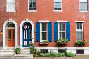 Red brick wall with blue window shutters and blue door. Colonial age brick building with plants on front steps. Historical building in Philadelphia United States.