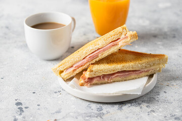 Ham and cheese sandwich, cup of coffee with milk and orange juice glass on concrete table in coffee...