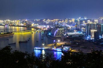 Night view of Sanya city with bright multi-colored illumination buildings, structures, roads, sidewalks, poles, bridges.