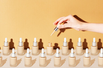 A female hand holds a dropper for applying bb foundation cream. Opened and closed jars of a cosmetic makeup product on a beige background. Pattern of beauty products packaging