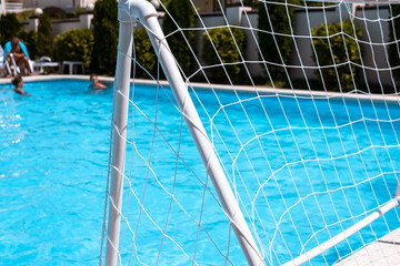 Fototapeta na wymiar White gate for water polo close-up on a background of a pool for relaxation. Water polo gate against the background of clear water in the pool with people.