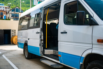 Tourist minibus is waiting with the door open in the parking lot. White minibus is parked in sunny weather.