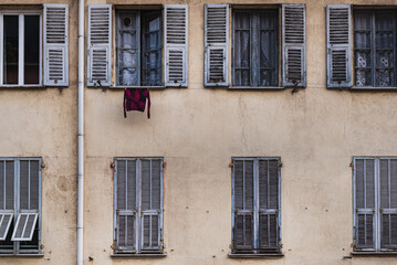 Hanging shirt at a window on a traditional old French facade with rows of open and closed louvered shutters (jalousie) conveys a downtown lifestyle and privacy, living together concept - Nice, France