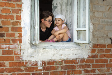 teen boy with glasses and little girl in the window of an old village house
