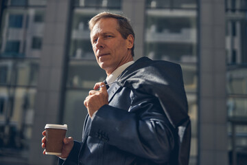 Good-looking man with cup of coffee standing on the street