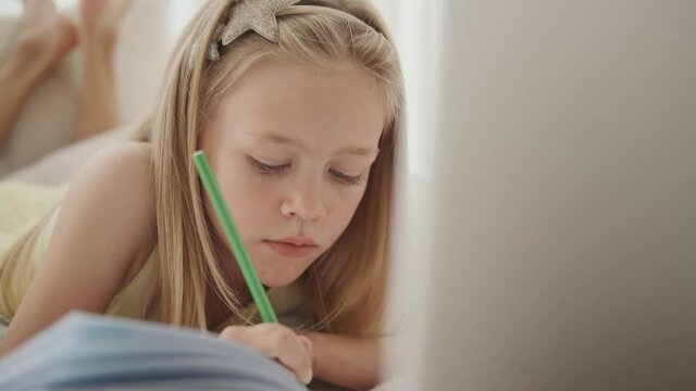 Little romantic girl writes in a diary at her bed