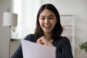 Excited Vietnamese millennial girl laugh reading good pleasant news in postal letter correspondence...
