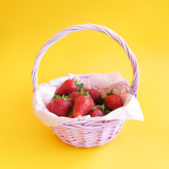 Ripe red strawberries in wicker basket on yellow background. Summer harvest. Fresh berries.