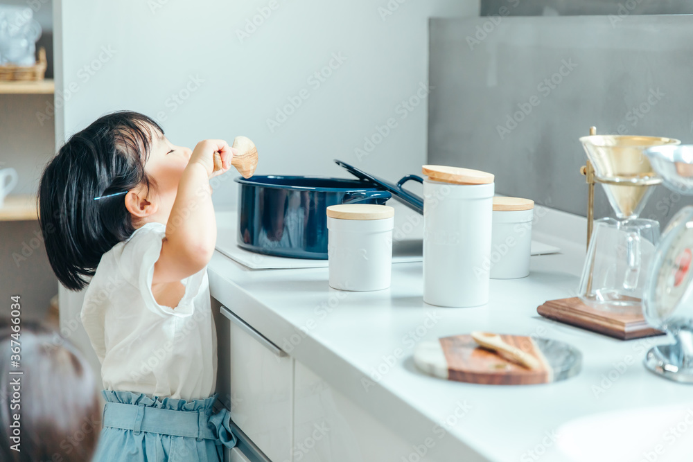 Wall mural 白いキッチンで女の子が鍋からつまみ食いをしている　kitchen girl eat