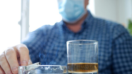 Man Wearing Protection Mask on His Face Drink a Glass with Alcohol in a Bar and Smoke a Cigarette