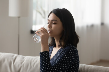 Thirsty Asian young woman drink clean clear pure mineral water from glass, feel dehydrated at home, millennial Vietnamese girl enjoy still aqua for refreshment, hydration, healthy lifestyle concept