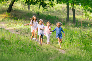 Fototapeta premium Kids, children running on meadow in summer's sunlight. Look happy, cheerful with sincere bright emotions. Cute caucasian boys and girls. Concept of childhood, happiness, movement, family and summer.
