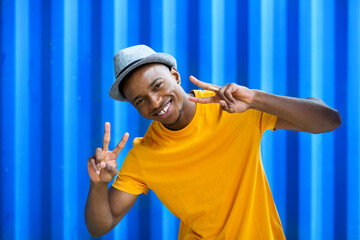 Cheerful young black man standing against blue background, peace gesture concept.