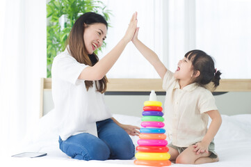 Obraz premium Happiness mother and daughter sit on a bed in the house doing high five while playing the colorful toy together, family joyful together in the house on holiday.