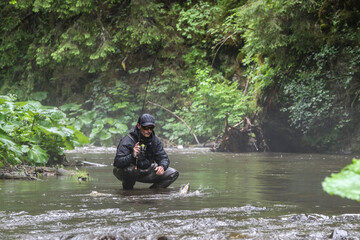 Fisherman hunting salmon fish. Outdoor fishing in river during rain. Hunting and hobby sport.