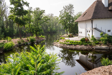 View of the river which reflects a white house with a reed roof and trees