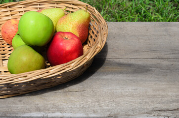 Ripe fruit in a wicker basket on a rough wooden surface. Apples and pears in a rustic style.