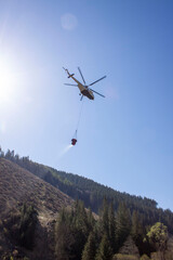 Fototapeta na wymiar Specially adapted helicopter with water extinguishing bag. Firefighting efforts are currently underway with helicopters to suppress forest fires