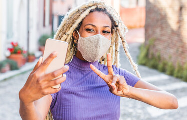Yound african woman with blond dreadlocks doing video call with smart mobile phone wearing face...