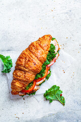 Croissant sandwich with meat, vegetables and green kale, white background. Breakfast food concept.