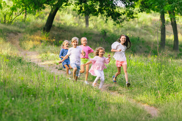 Fototapeta premium Kids, children running on meadow in summer's sunlight. Look happy, cheerful with sincere bright emotions. Cute caucasian boys and girls. Concept of childhood, happiness, movement, family and summer.