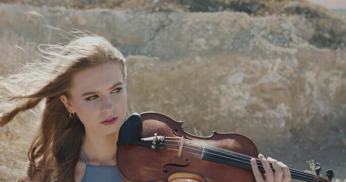 View of elegant woman stands on cliff anf starts to play violin