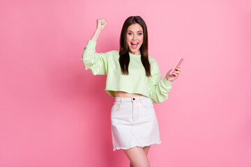 Photo of charming excited lady hold telephone read good news blog new followers subscribers popularity wear casual green crop pullover jeans skirt isolated pink pastel color background