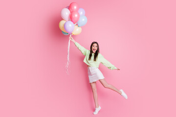 Full size photo of charming lady hold many air balloons rise up air flying overjoyed excited wear casual green crop pullover jeans mini skirt shoes isolated pink pastel color background