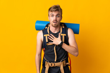 Young mountaineer man with a big backpack isolated on yellow background surprised and shocked while looking right