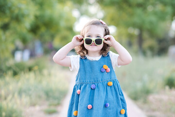 Cute baby girl 2-3 year old having fun outdoors over green nature background closeup. Looking at camera. Childhood.