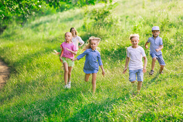 Fototapeta premium Kids, children running on meadow in summer's sunlight. Look happy, cheerful with sincere bright emotions. Cute caucasian boys and girls. Concept of childhood, happiness, movement, family and summer.
