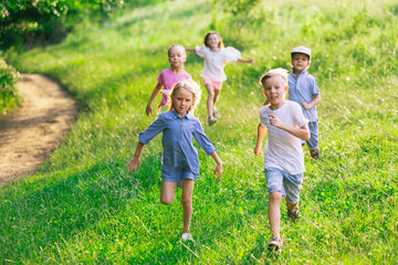 Fototapeta premium Kids, children running on meadow in summer's sunlight. Look happy, cheerful with sincere bright emotions. Cute caucasian boys and girls. Concept of childhood, happiness, movement, family and summer.