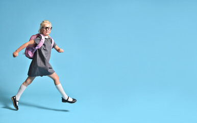 A junior schoolgirl with a backpack runs cheerfully on a blue background