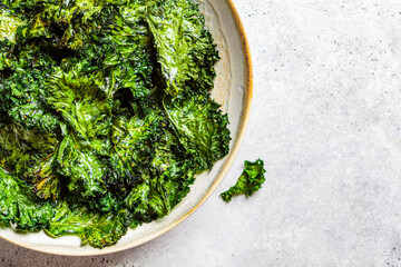 Green kale chips with salt in a white dish, top view. Healthy vegan food concept.