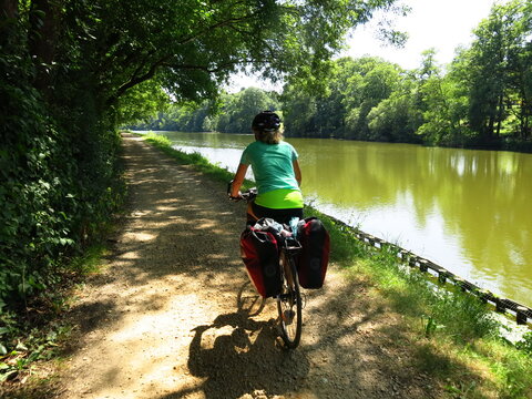 Jeune femme cycliste à vélo avec sacoche sur piste cyclable pour randonnée bicyclette le long d'un canal d'eau de rivière en France dans la Loire