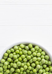 Green peas on a white table with copy space for text. Fresh harvest from the garden. Shelled green peas in a white bowl. Minimal concept, close-up