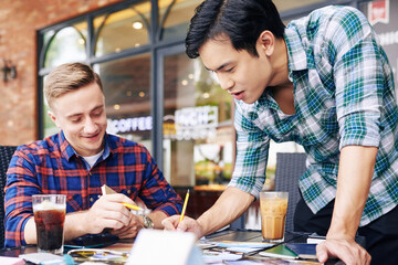 Fototapeta premium Photographers discussing printed out photos when meeting in outdoor cafe