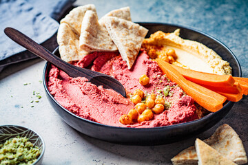Beetroot hummus and classic hummus in black dish with carrots and pita bread. Plant based diet concept.