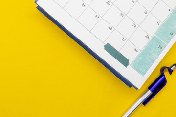 Calendar with pen placed on a yellow table. There is space for text. Business or travel trip concept.