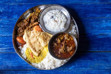 Rice with Goat Curry and Other Dishes in Steel Plate on Blue Wooden Background, Typical Bengali Food Platter or Thali