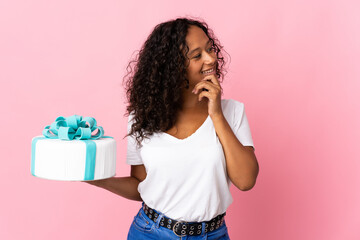 Pastry chef holding a big cake isolated on pink background thinking an idea and looking side