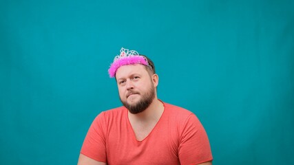 Playful bearded freaky man in a pink T-shirt with a deadema on his head sad with a magic wand in...