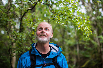 Naklejka na ściany i meble A portrait of a happy older man ,looking up into the sky, in a forest