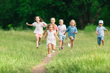 Kids, children running on meadow in summer's sunlight. Look happy, cheerful with sincere bright emotions. Cute caucasian boys and girls. Concept of childhood, happiness, movement, family and summer.