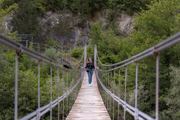 A young woman crossing a scary and narrow suspension bridge over a cold river.