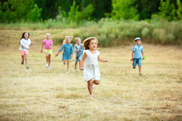 Kids, children running on meadow in summer's sunlight. Look happy, cheerful with sincere bright emotions. Cute caucasian boys and girls. Concept of childhood, happiness, movement, family and summer.