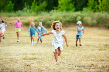 Kids, children running on meadow in summer's sunlight. Look happy, cheerful with sincere bright emotions. Cute caucasian boys and girls. Concept of childhood, happiness, movement, family and summer.